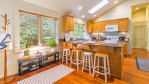 A modern kitchen with wooden cabinets, a central island with stools, a microwave, and a stove. - The Cottage at Herons Roost by AvantStay (Langley)