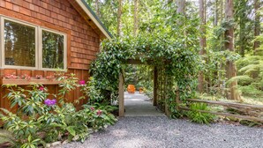 A wooden cabin with a gravel path leading to a wooden archway covered in greenery. - The Cottage at Herons Roost by AvantStay (Langley)