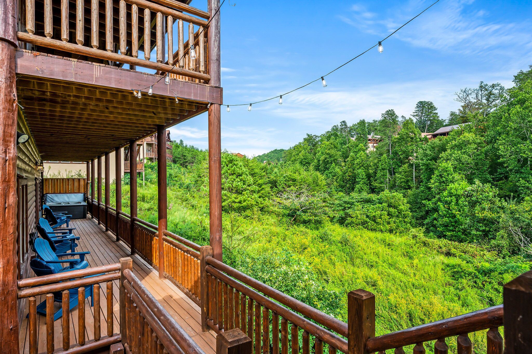 Una terraza de madera con sillas y un sofá azules, con vistas a un bosque verde y frondoso.