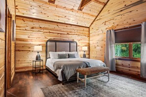 A wooden cabin bedroom with a bed, bedside lamps, a bench, and a window with curtains.