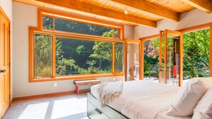 A bedroom with a large window, a bed, a bench, and a view of greenery. - Rhythm Waters by AvantStay | Garden Paradise, Pond (Langley)