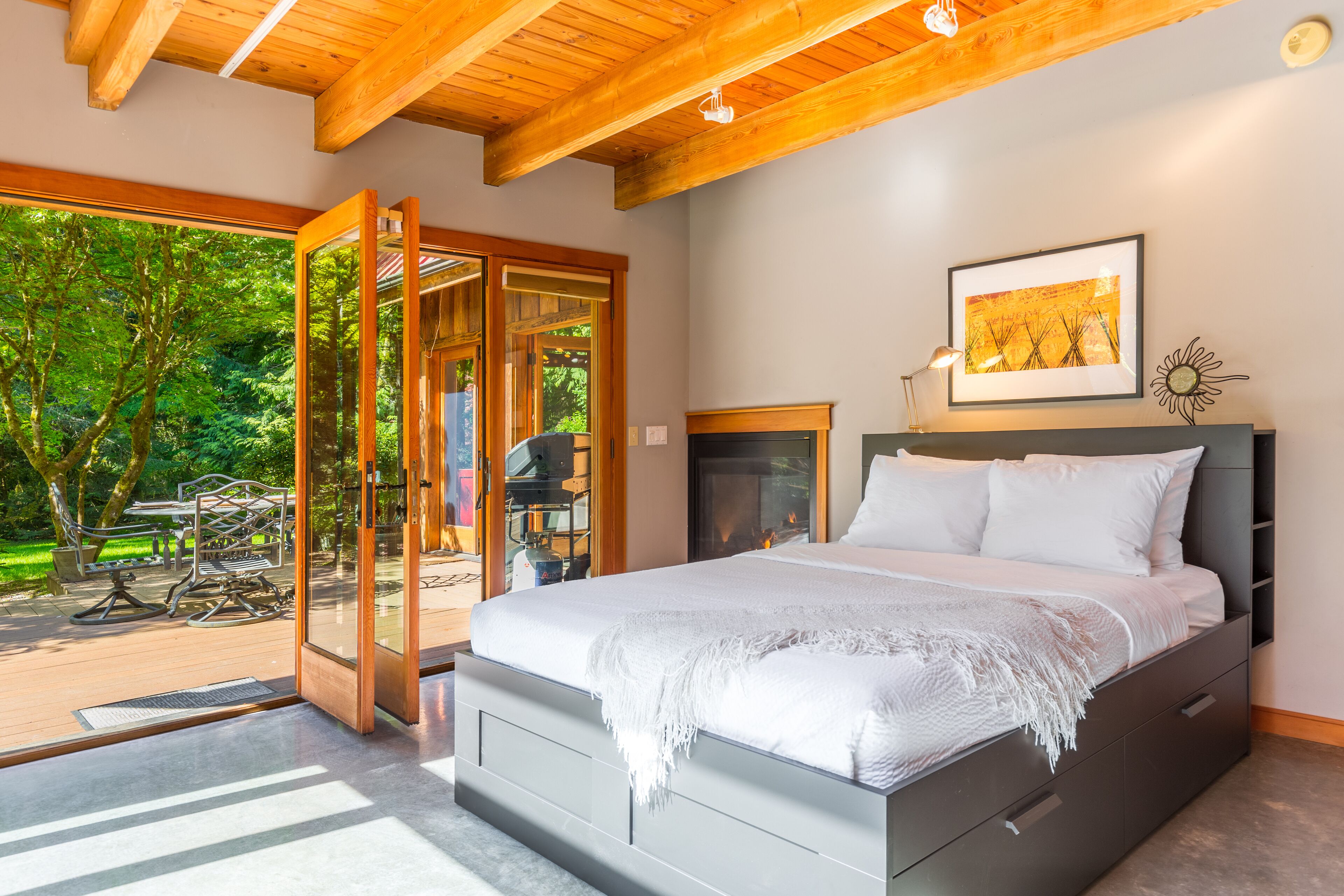 Un dormitorio moderno con una cama grande, una chimenea y vistas a una terraza y árboles.