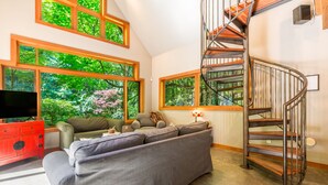 A living room with a grey sofa, a red cabinet, a TV, and a spiral staircase. - Rhythm Waters by AvantStay | Garden Paradise, Pond (Langley)
