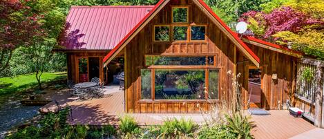 A wooden cabin with a red roof, large windows, and a deck.