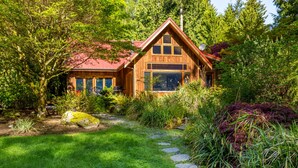 A wooden cabin with a red roof, surrounded by lush greenery and a stone pathway. - Rhythm Waters by AvantStay | Garden Paradise, Pond (Langley)