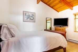 Une chambre à coucher avec un lit, un téléviseur posé sur une commode en bois et un tableau encadré accroché au mur.