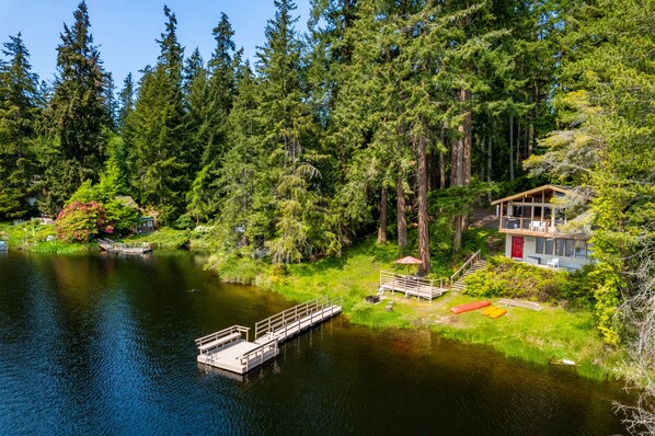 Un chalet au bord du lac, doté d’un quai, et entouré d’une forêt dense.