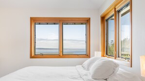 Een slaapkamer met een bed, een raam met uitzicht op zee en een nachtkastje.