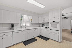Eine moderne Küche mit weißen Schränken, einer Mikrowelle, einer Kaffeemaschine und einem Deckenventilator.