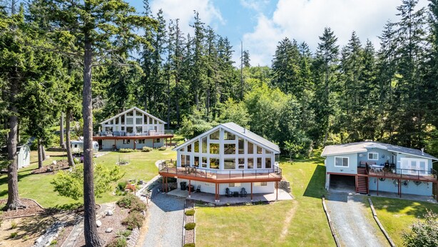 Ein modernes, zweistöckiges Haus mit einer großen Terrasse und einer überdachten Außenbereich, umgeben von bewaldeter Landschaft.