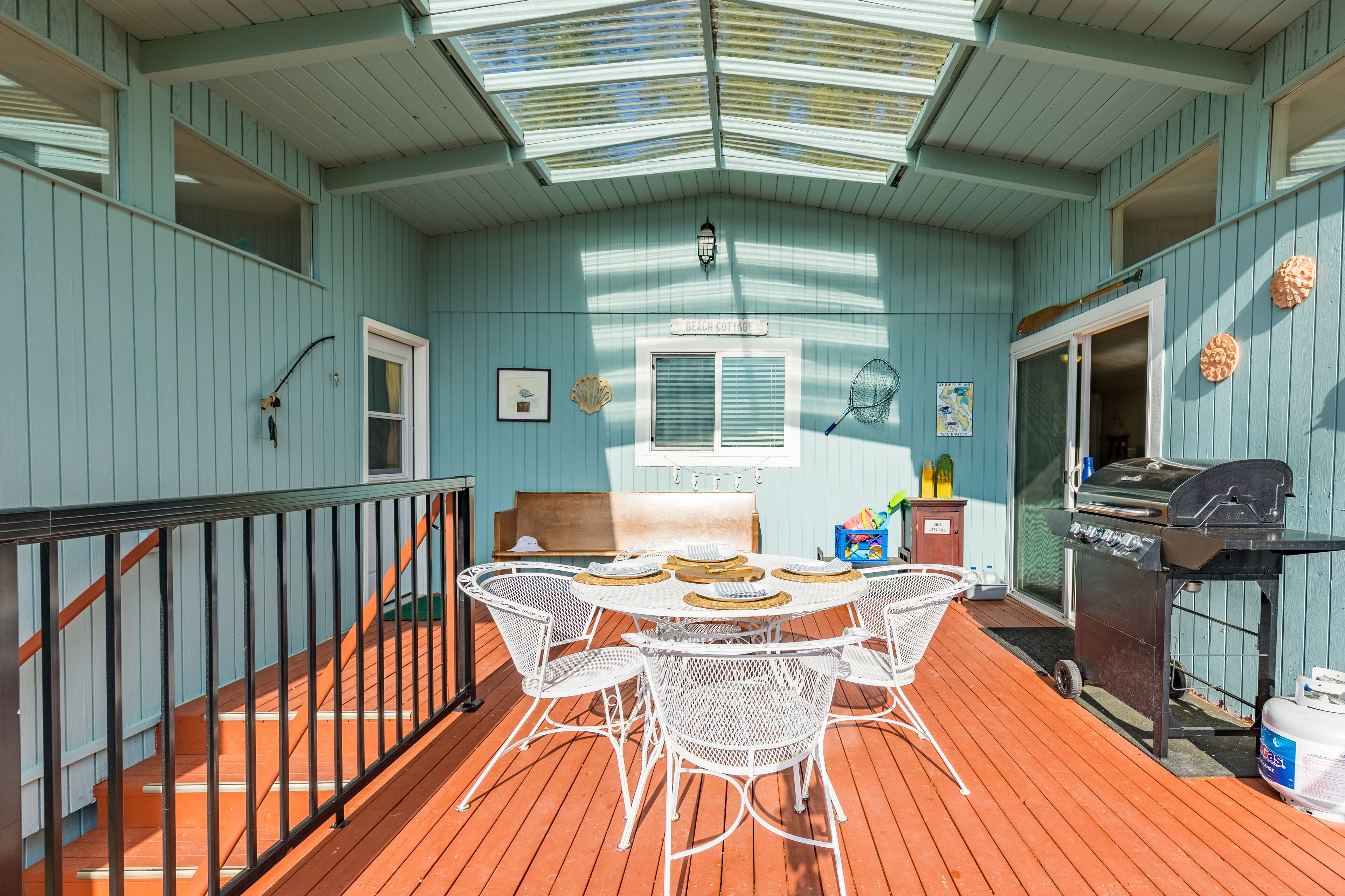 A covered deck with a table and chairs, a grill, and a small seating area with a bench.