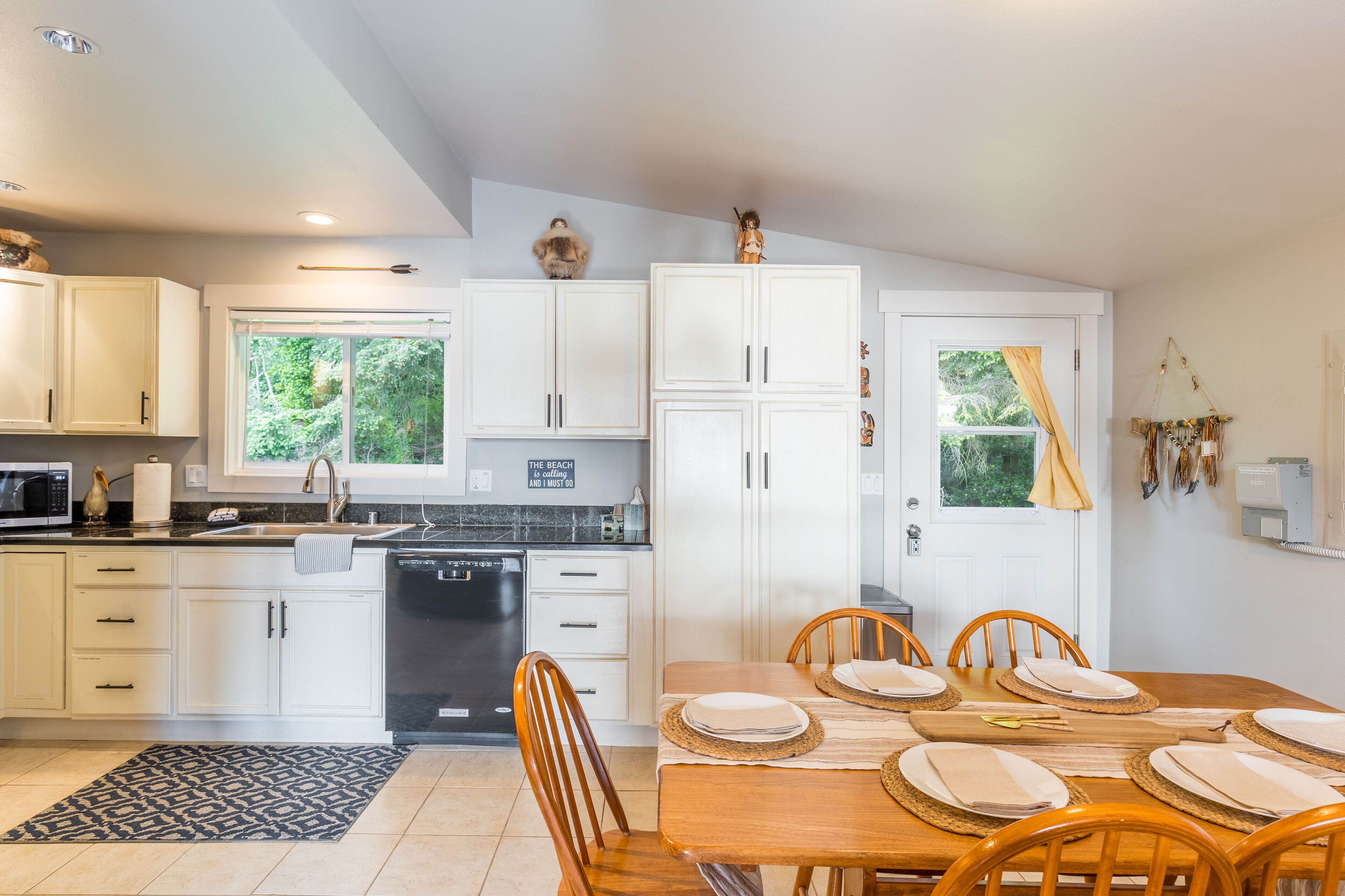 Une cuisine moderne avec des meubles blancs, une table à manger pour quatre personnes et une vue sur la verdure à l’extérieur.