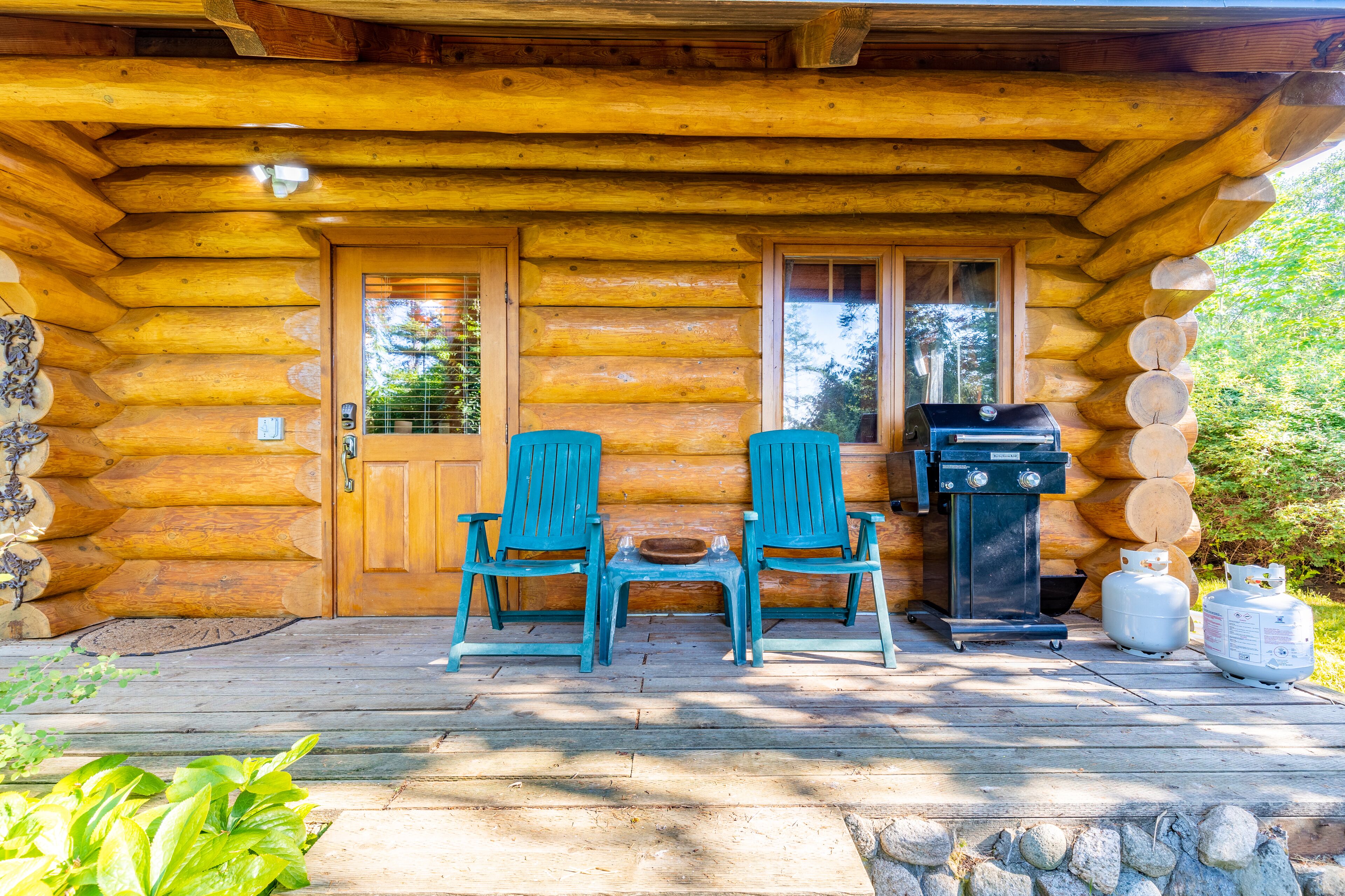 A log cabin with two blue chairs and a grill outside.