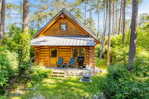 A log cabin with two chairs on the porch, a grill, and a stone fireplace. - Penn Cove Overlook by AvantStay | Cabin w/ Views (Oak Harbor)