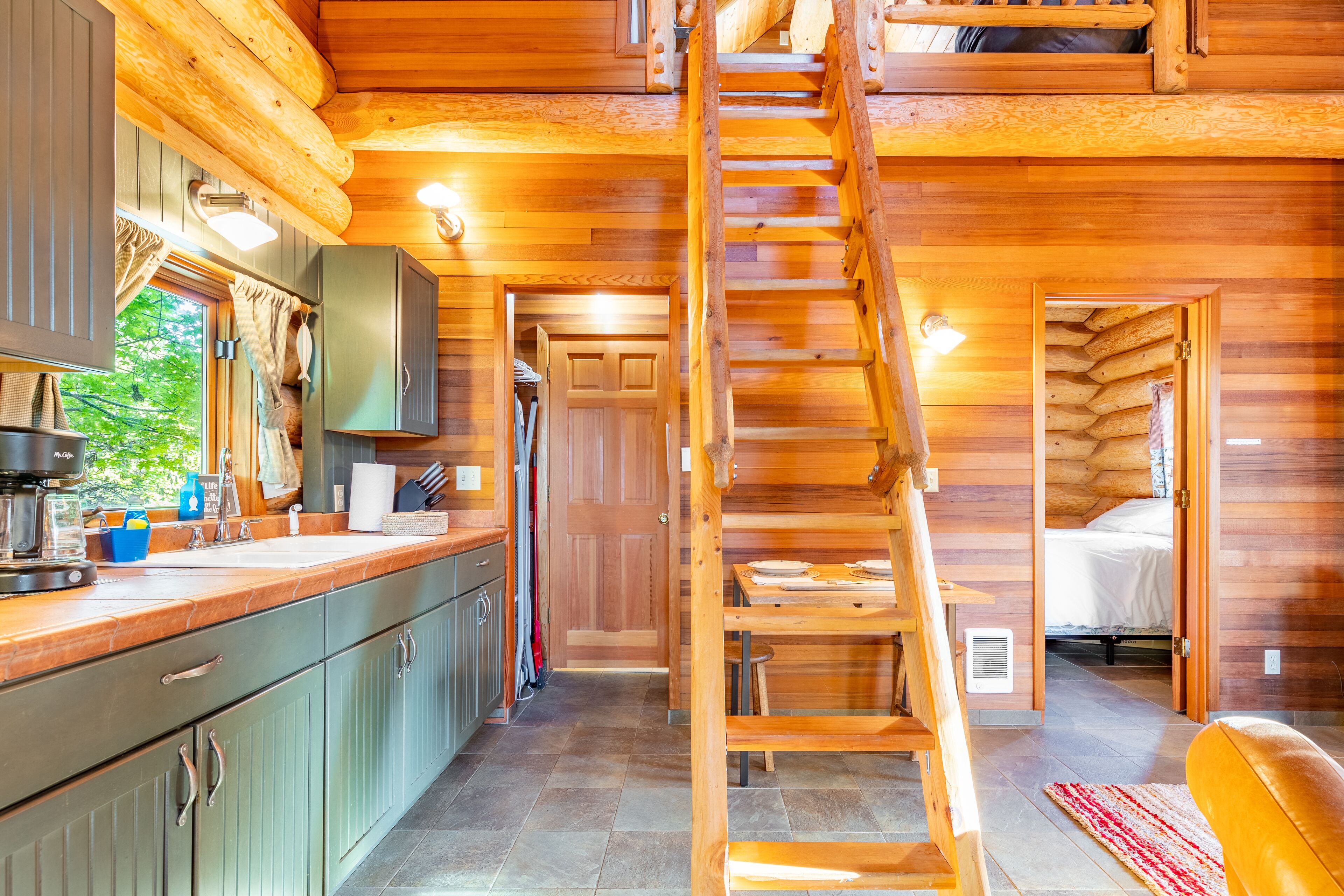 L’intérieur d’une cabane en rondins comprend une cuisine, un coin repas et une chambre à coucher. Un escalier en bois relie les différents espaces.
