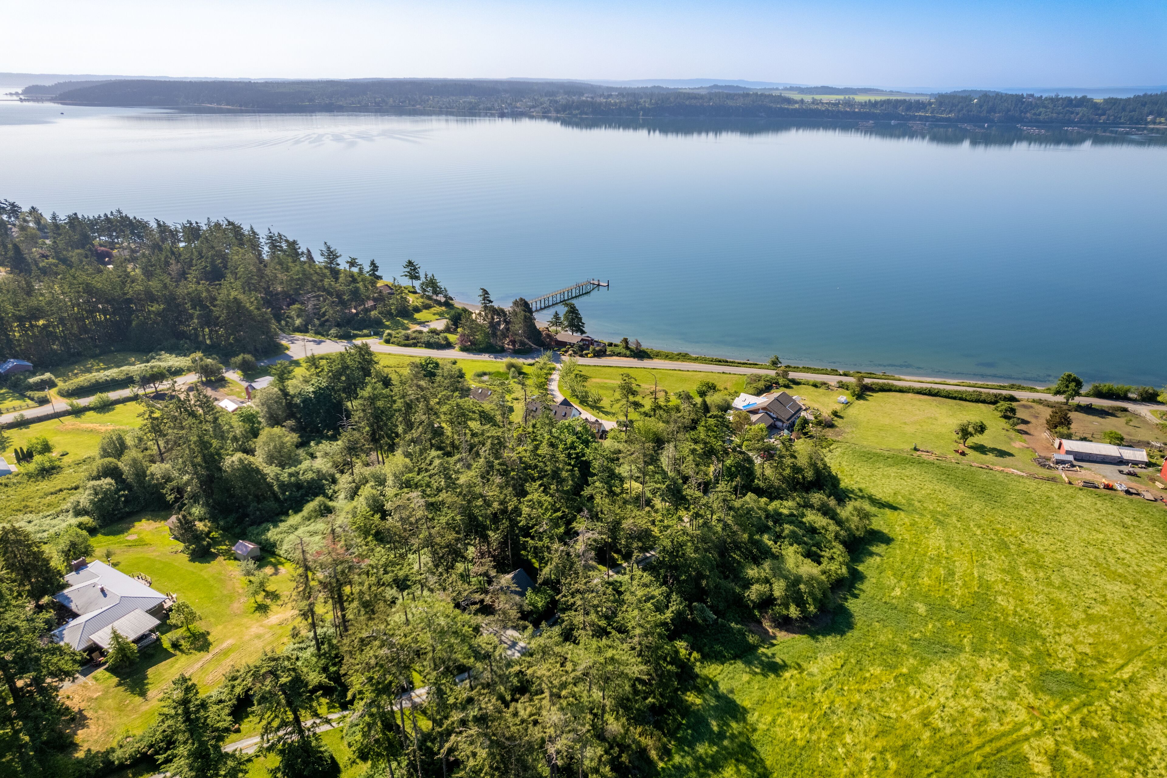 An aerial view of a lakeside property with a dock, surrounded by dense forest and open grassy areas.