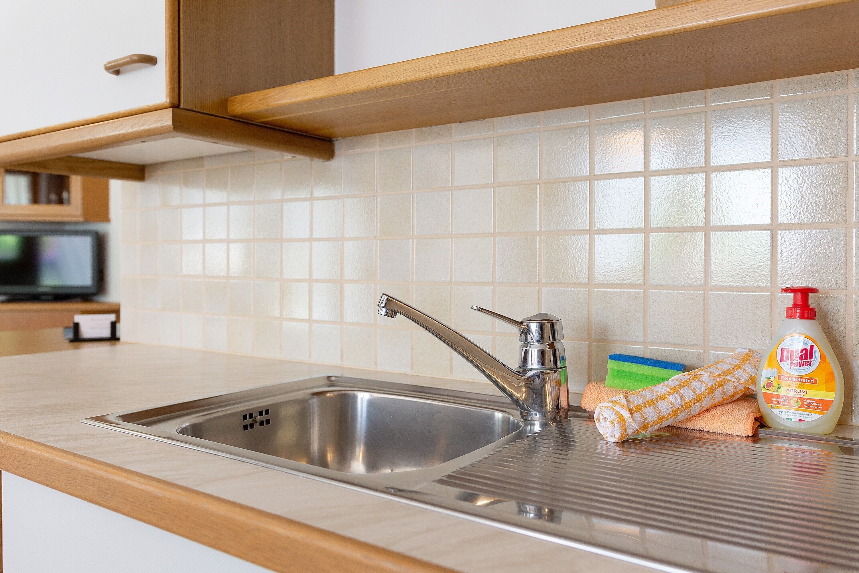 A kitchen with a stainless steel sink, a soap dispenser, and a towel.
