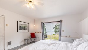 Un dormitorio con una cama grande, un ventilador de techo, una ventana con vistas al exterior y una silla con un cojín rojo.