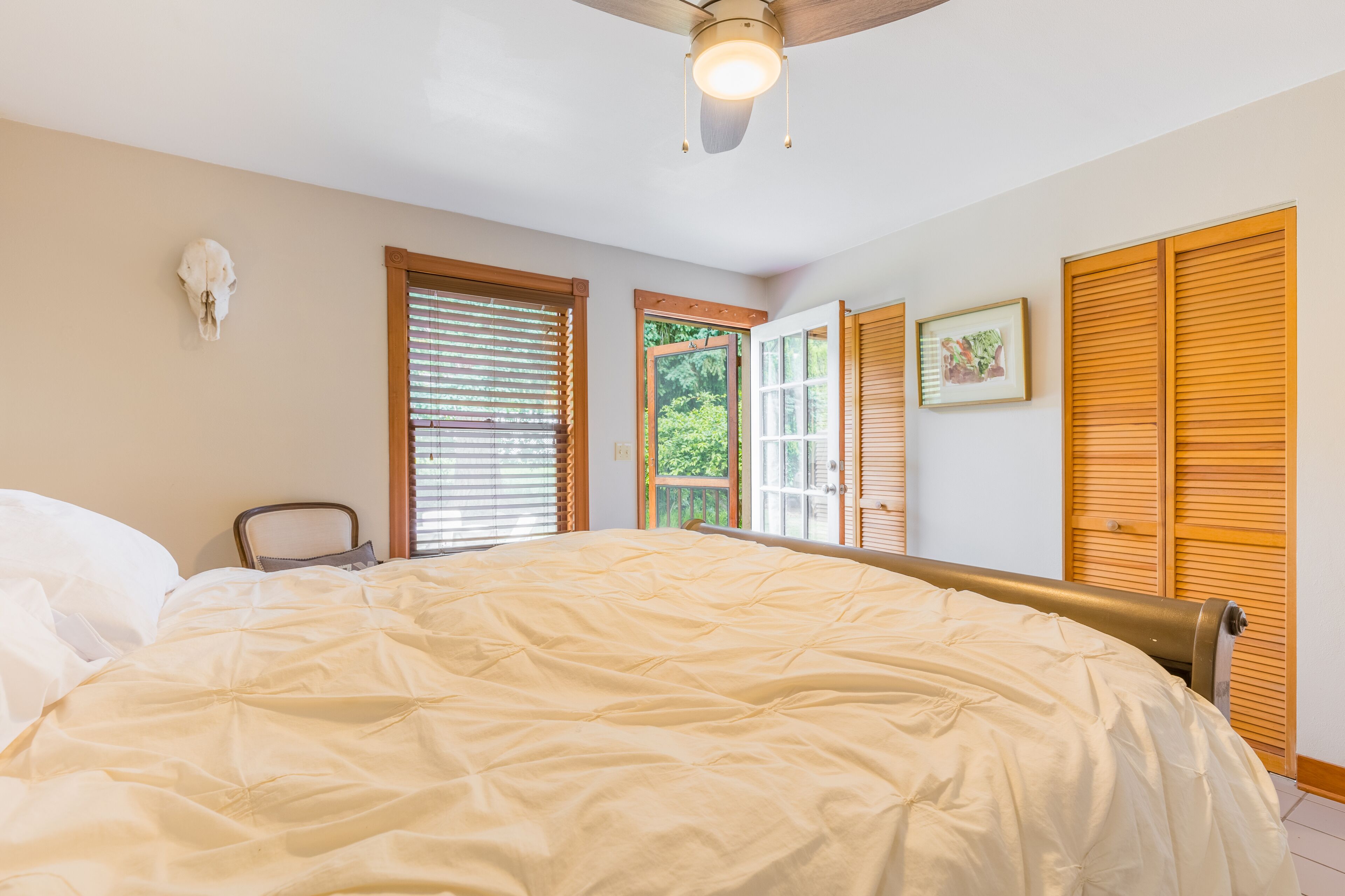 A bedroom with a large bed, wooden shutters, a ceiling fan, and a window with blinds.