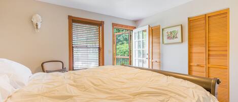 A bedroom with a large bed, wooden shutters, a ceiling fan, and a window with blinds.