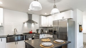 A modern kitchen with white cabinets, stainless steel appliances, and a central island with placemats. - Twin Oaks Retreat by AvantStay | Mins to Freeland (Freeland)
