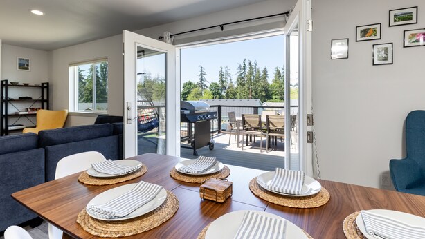 A dining area with a wooden table set for four, a sofa, and a grill outside. - Twin Oaks Retreat by AvantStay | Mins to Freeland (Freeland)