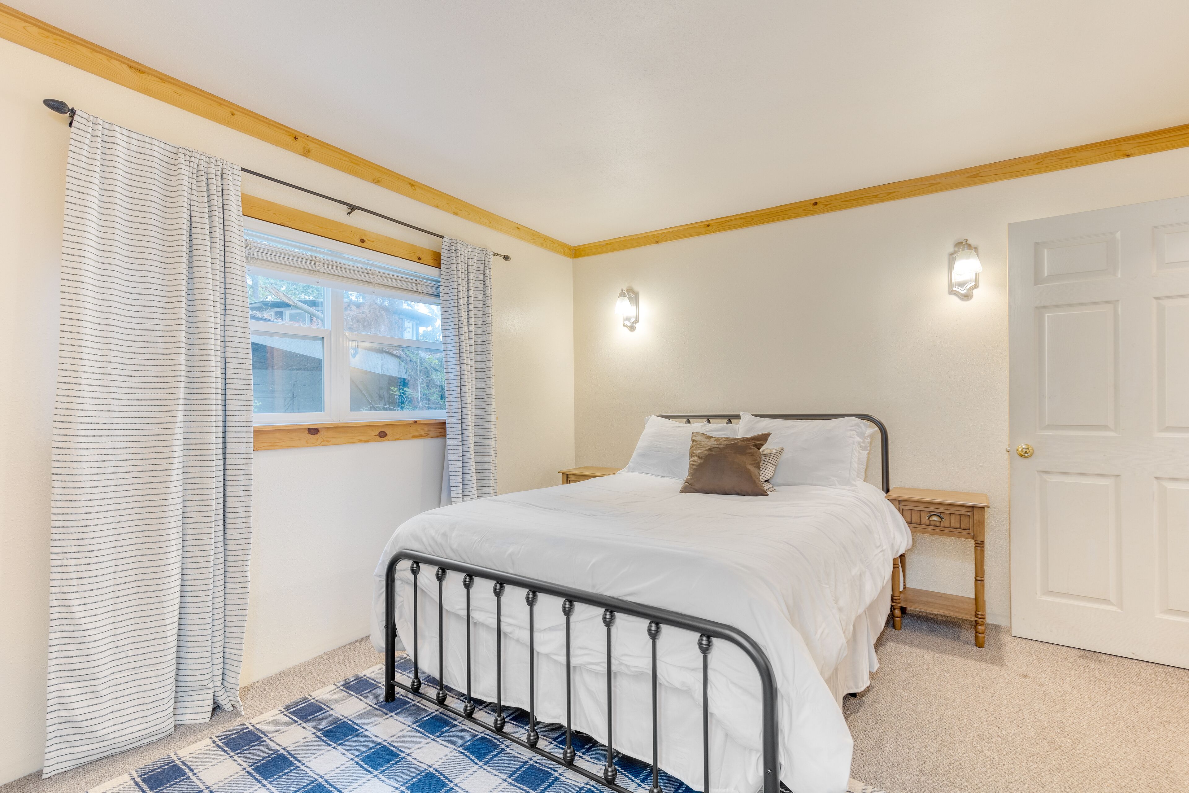 Un dormitorio con cama, mesita de noche, ventana con cortinas y puerta.
