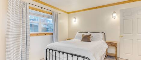 Un dormitorio con cama, mesita de noche, ventana con cortinas y puerta.