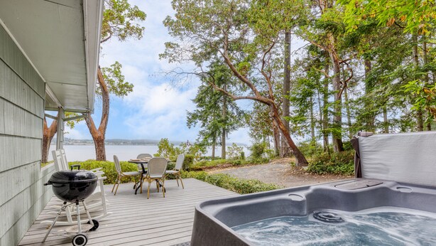 En terrasse med jacuzzi, grill og udendørs møbler med udsigt over vand.