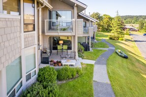Una casa moderna de dos pisos con un balcón, un patio con mobiliario exterior y un césped bien cuidado.