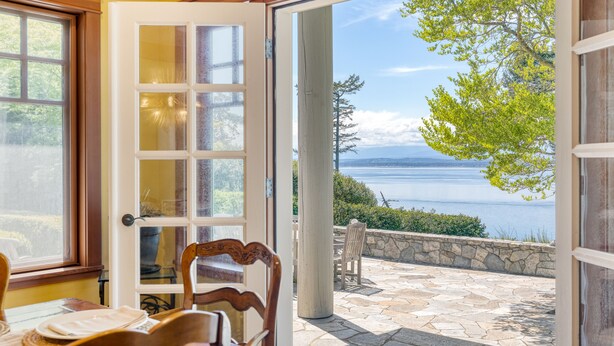 A room with a large glass door leading to a patio with stone flooring and a view of a lake.