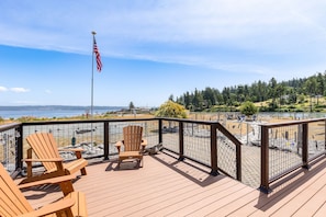 Enjoy the serene waterfront view from this deck, featuring two Adirondack chairs and a flag.
