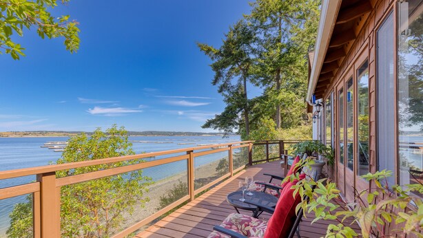 Eine Holzterrasse mit Seeblick, ausgestattet mit Stühlen und einem Tisch, die auf das Wasser blickt.