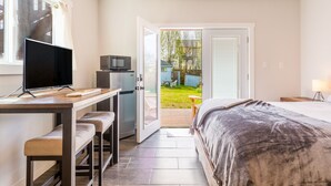 A bedroom with a bed, a desk with a TV, a microwave, and a sliding door to a balcony. - Lagoon Point Retreat • Beach Access + Fire Pit + Game Room | Chateau Coho (Greenbank)