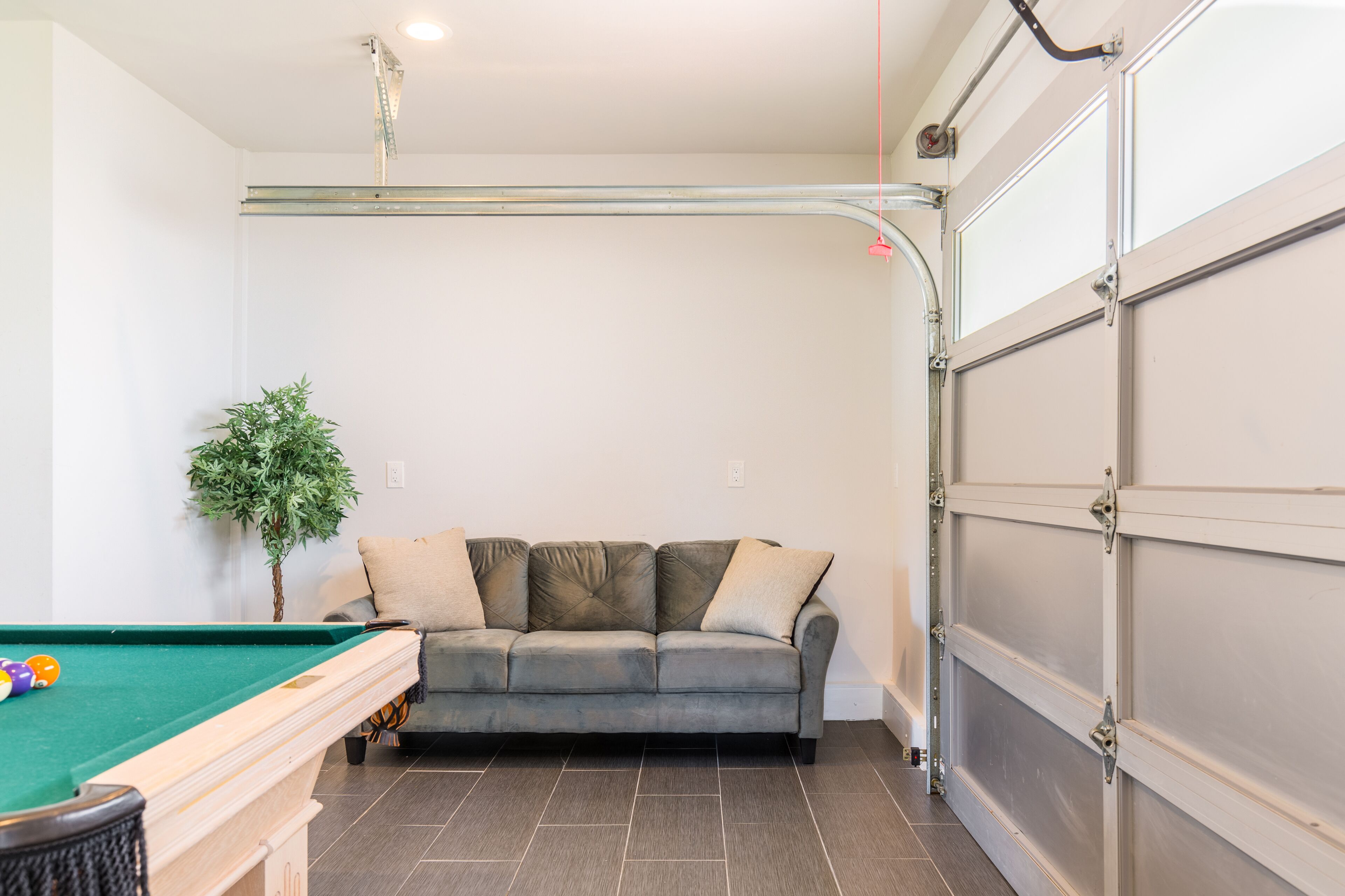 Una habitación con mesa de billar, sofá y puerta de garaje.