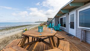 A wooden deck with a table and chairs, overlooking a beach. - West Beach Wonderland by AvantStay | Waterfront (Oak Harbor)