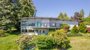 A two-story house with a balcony, surrounded by lush greenery and trees. - Sunny Side Island Retreat by AvantStay | Backyard (Freeland)