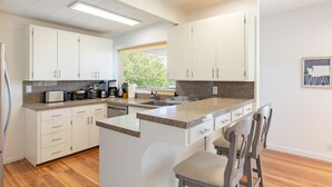 A modern kitchen with white cabinets, granite countertops, and a central island with bar stools. - Sunny Side Island Retreat by AvantStay | Backyard (Freeland)
