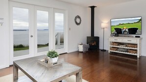 A living room with a fireplace, a television, and a view of the water. - Marine View Bluff by AvantStay | Waterfront Views (Greenbank)