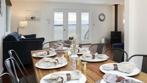 A dining area with a wooden table set for four, white plates, folded napkins, and a vase with flowers. - Marine View Bluff by AvantStay | Waterfront Views (Greenbank)