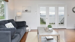 A modern living room with a grey sofa, a wooden coffee table, and a view of a body of water through large glass doors. - Marine View Bluff by AvantStay | Waterfront Views (Greenbank)
