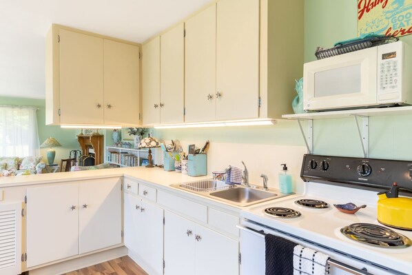 Una cocina con armarios blancos, un microondas, una estufa y diversos utensilios de cocina.