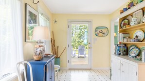 Ein Zimmer mit einer Tür zu einem Außenbereich, einem blauen Schrank, einem weißen Stuhl und einem Regal mit Geschirr und Büchern.