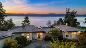A two-story house with a view of a lake at sunset.