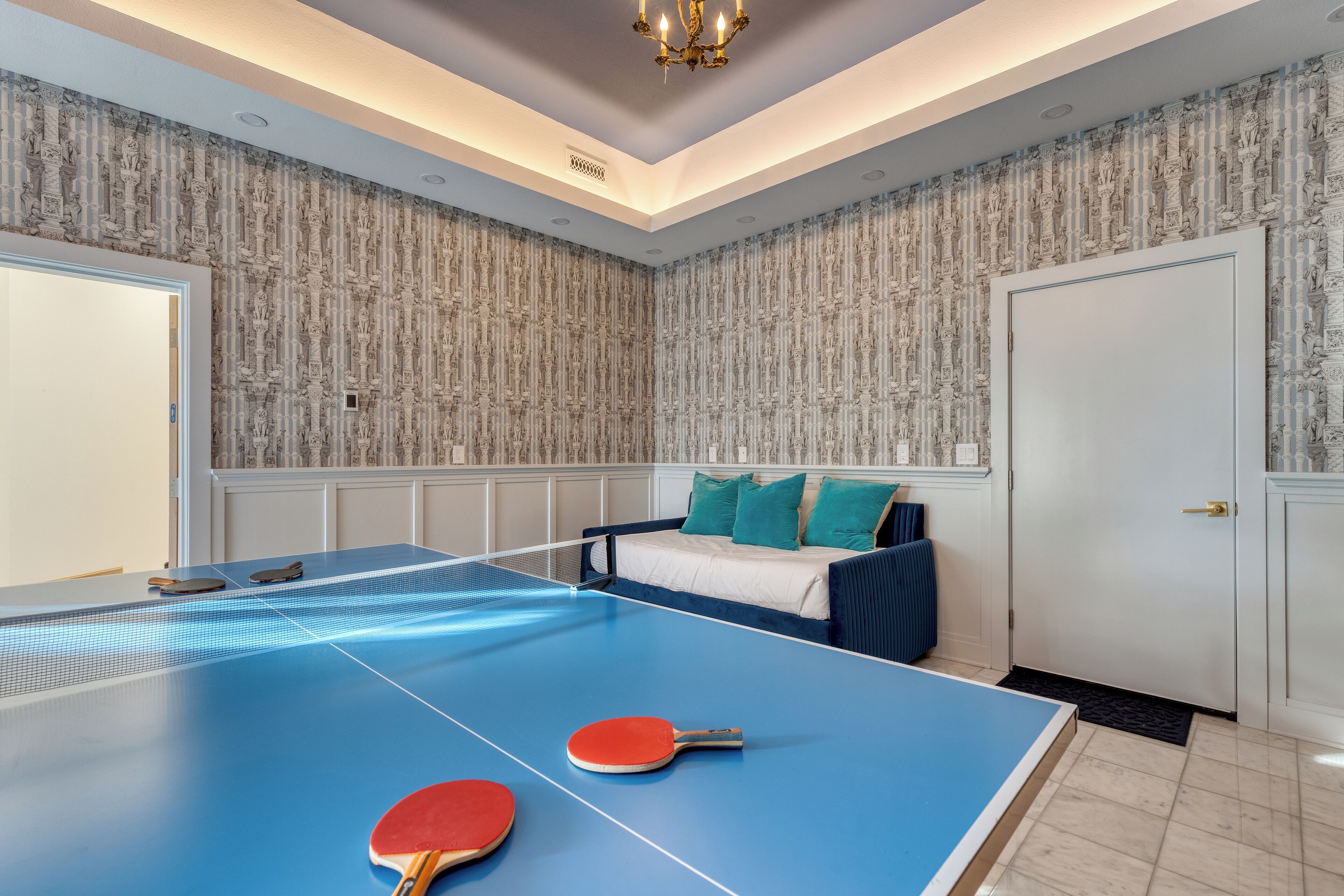 A room with a ping pong table, a bed with blue bedding, and a patterned wallpaper.