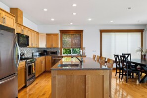 Una cocina moderna con armarios de madera, electrodomésticos de acero inoxidable, una isla central y un comedor con sillas.