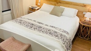 Un dormitorio ordenado con cama, mesitas de noche, lámpara colgante, un taburete y ventilador de techo.