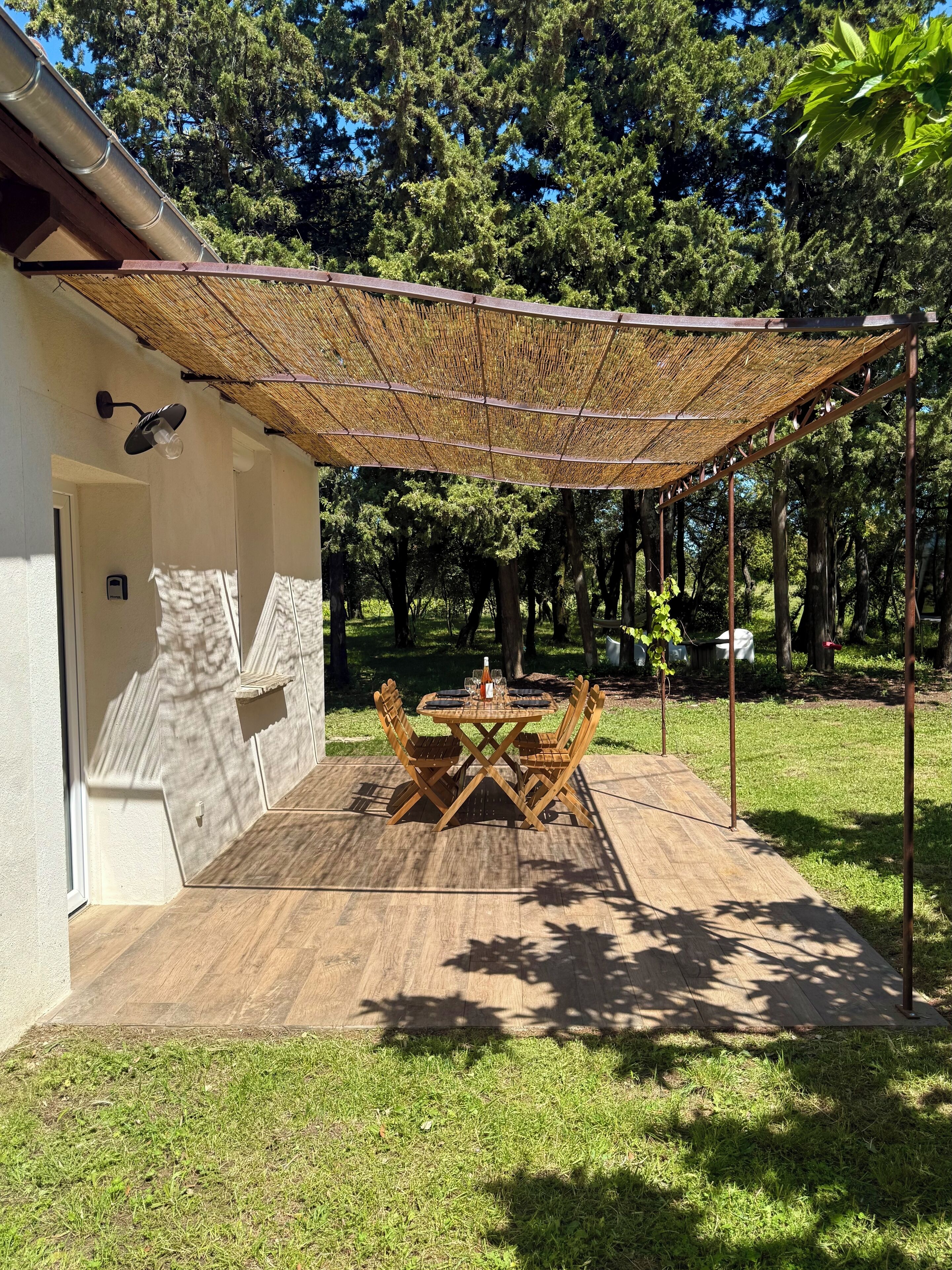 A covered patio with a table and chairs, surrounded by a grassy area and trees.