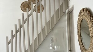 Una escalera con barandilla blanca, un interruptor de luz en la pared y un espejo decorativo con marco tejido.