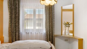 Une chambre d’hôtel avec un lit, des rideaux, un miroir et un vase rempli de fleurs, posé sur une étagère.